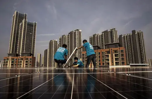 Three workers install a solar panel on the roof of a building in Wuhan, China.